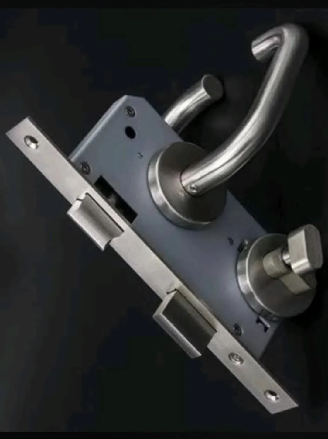 Cerradura embutida de acero con manilla y pomo de seguridad, vista de frente con el frontal y los resbalones a la vista.