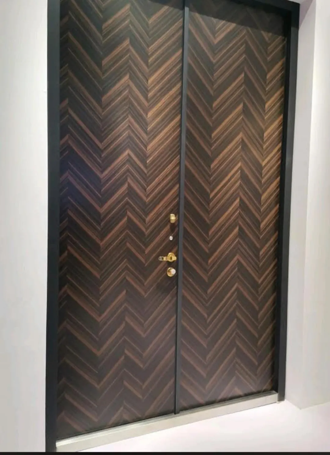 Puerta acorazada de dos hojas con acabado de madera en espiga y cerco metálico negro.