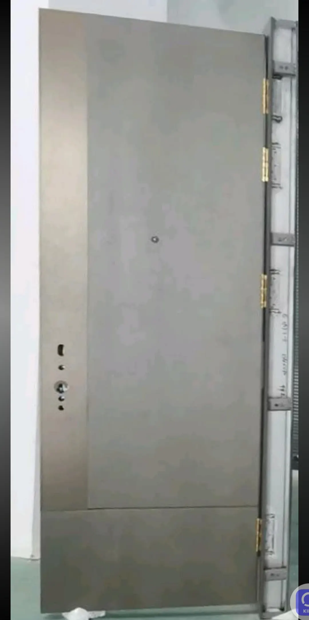 Puerta blindada gris con los taladros de la cerradura y la mirilla, junto a su cerco de acero.