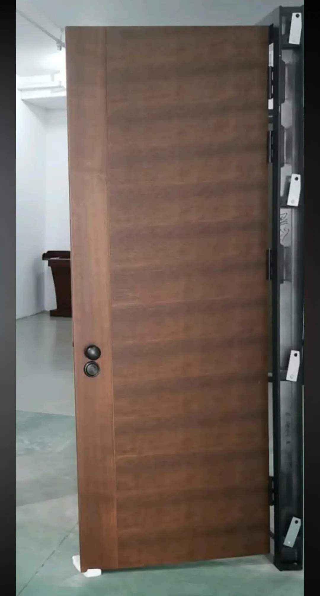Puerta blindada con acabado de madera en tono nogal y pomo fijo, apoyada junto a su cerco.