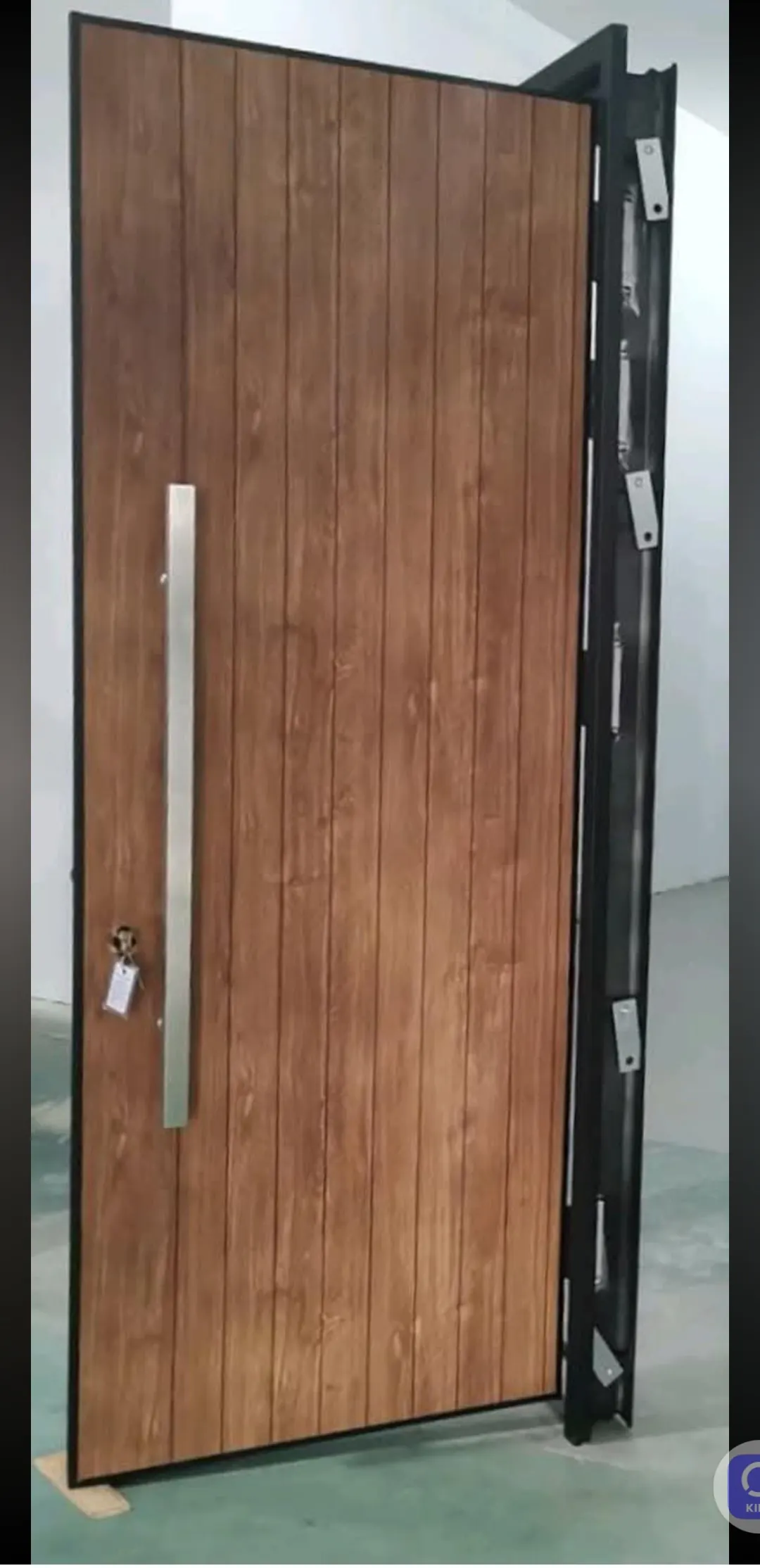 Puerta blindada con acabado de madera vertical y tirador largo de acero, abierta y con el cerco reforzado a la vista.